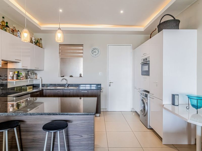 Modern kitchen featuring sleek white and wood-grain cabinetry, granite countertops, integrated appliances, and recessed ceiling lighting with a breakfast bar area.