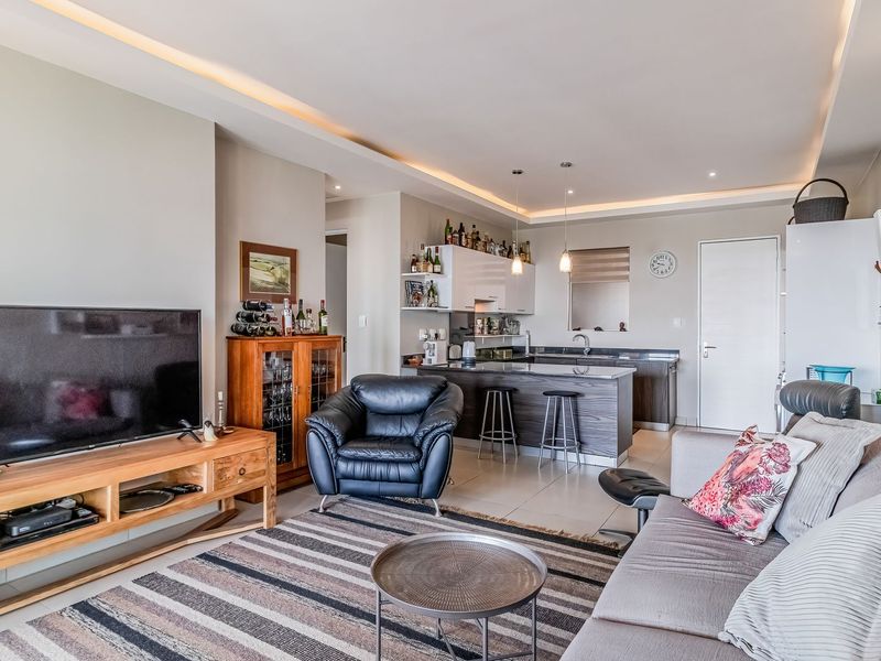 Spacious open-plan living area featuring a modern kitchen with an island, recessed ceiling lighting, and neutral tiled flooring throughout.
