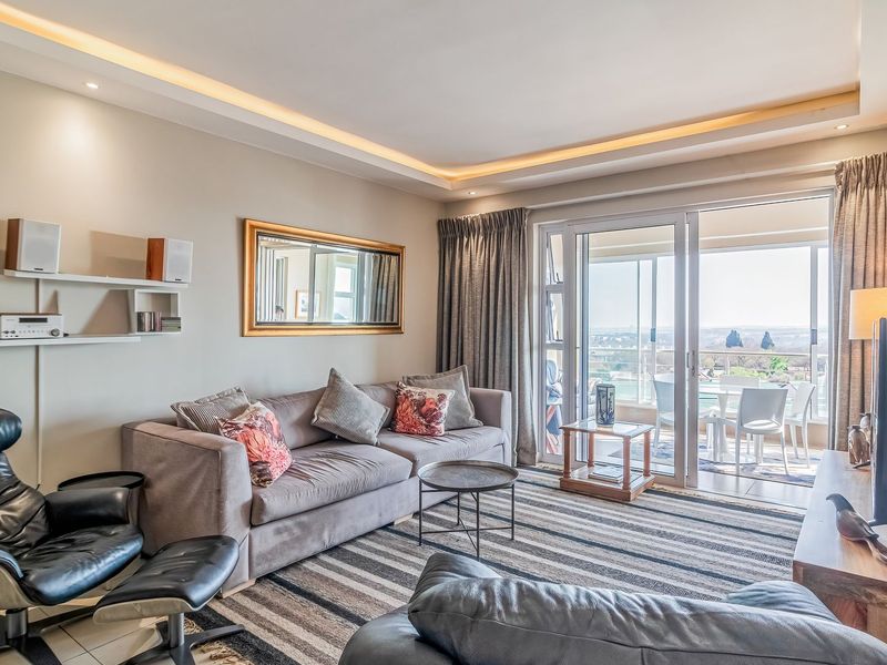 A well-maintained living room featuring recessed ceiling lighting, tiled floors, and large sliding glass doors providing access to a balcony with scenic views.