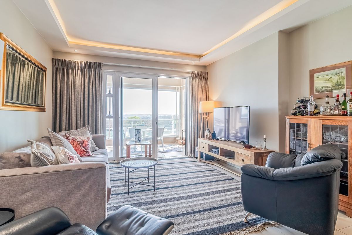 A bright and well-maintained living room featuring recessed ceiling lighting, tiled floors, and large sliding glass doors leading to an outdoor balcony.