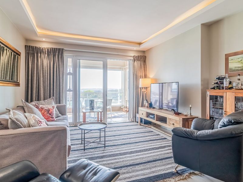 A bright and well-maintained living room featuring recessed ceiling lighting, tiled floors, and large sliding glass doors leading to an outdoor balcony.