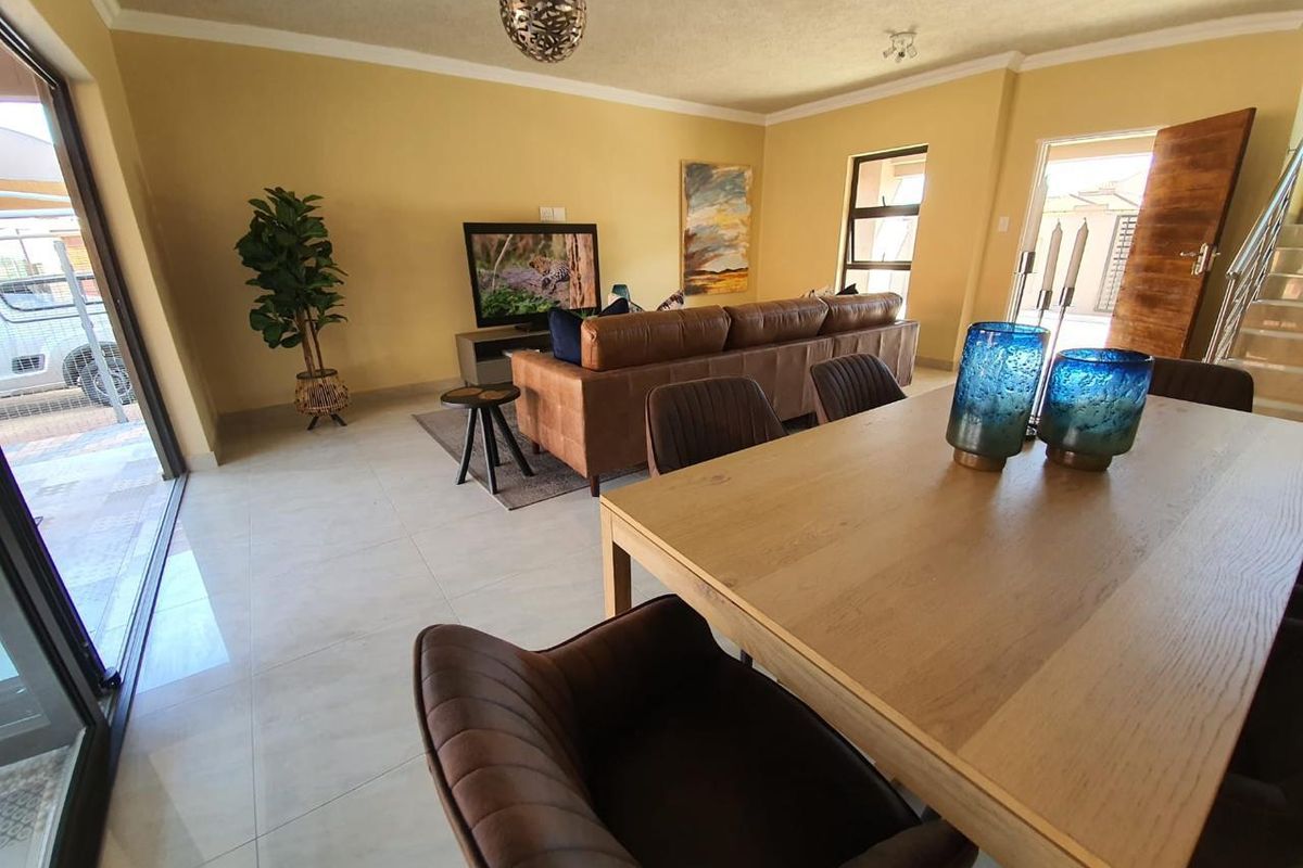An open-plan living and dining area featuring large format floor tiles, a sliding glass door to the exterior, and an internal staircase.