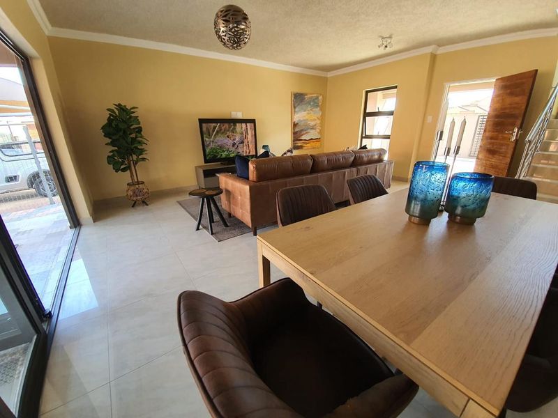 An open-plan living and dining area featuring large format floor tiles, a sliding glass door to the exterior, and an internal staircase.