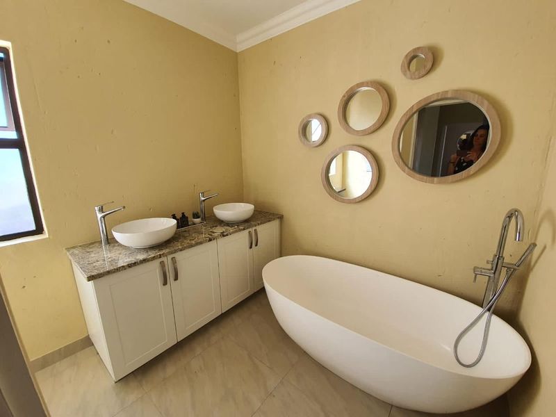 Modern bathroom featuring a double vanity with granite countertops, vessel sinks, and a contemporary freestanding bathtub with a floor-mounted mixer.