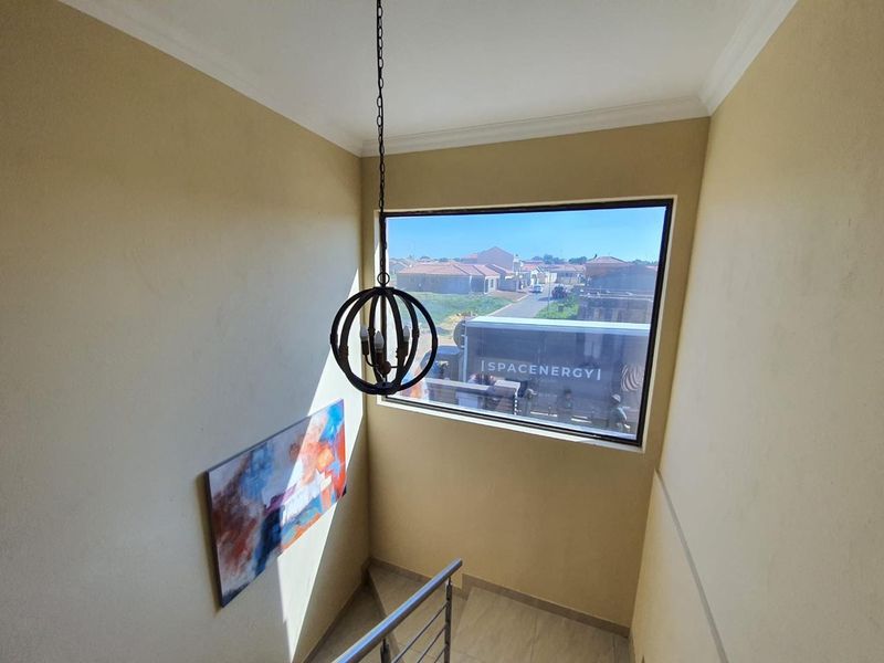 A bright staircase landing featuring a large window with neighborhood views, a modern pendant light, and neutral wall finishes.