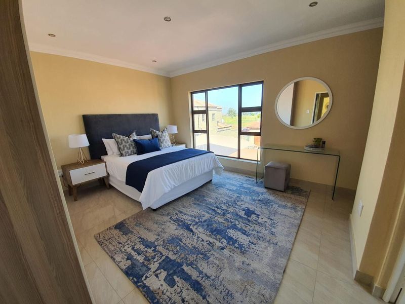 A well-lit, spacious bedroom featuring neutral wall tones, tiled flooring, and a large window providing natural light and exterior views.