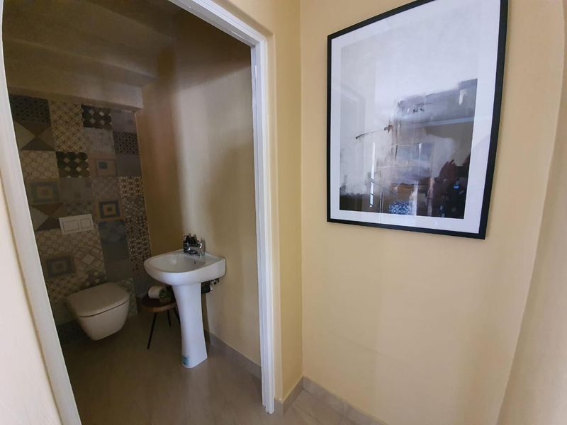 A compact guest bathroom featuring a modern wall-hung toilet, a pedestal basin, and decorative patterned wall tiling.