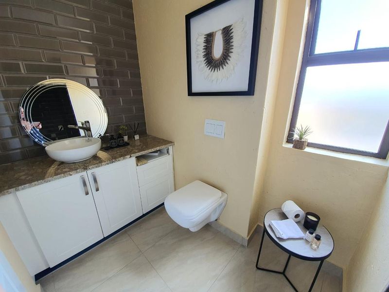 A modern bathroom featuring a wall-mounted toilet, a vanity cabinet with a stone countertop, and a stylish vessel sink with subway tile backsplash.