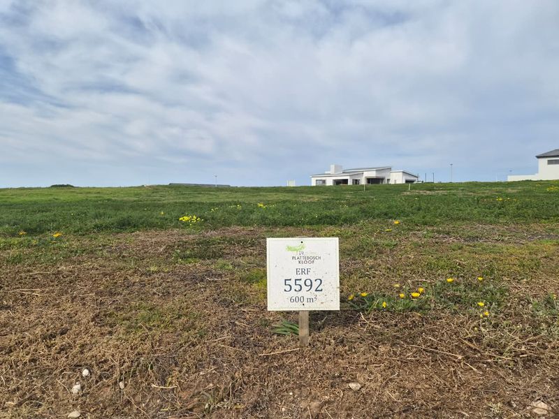 A vacant residential plot of 600 square meters in Plattebosch Kloof, featuring open grass terrain and clear property identification signage.