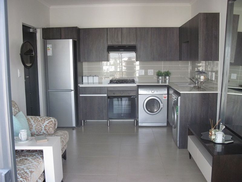 Modern open-plan kitchen featuring dark wood cabinetry, integrated appliances, tiled backsplash, and neutral floor tiles, seamlessly connecting to the living area.