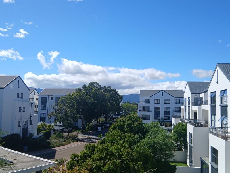 An elevated view overlooking a modern residential apartment complex with white facades, pitched roofs, and landscaped surroundings under a clear blue sky.