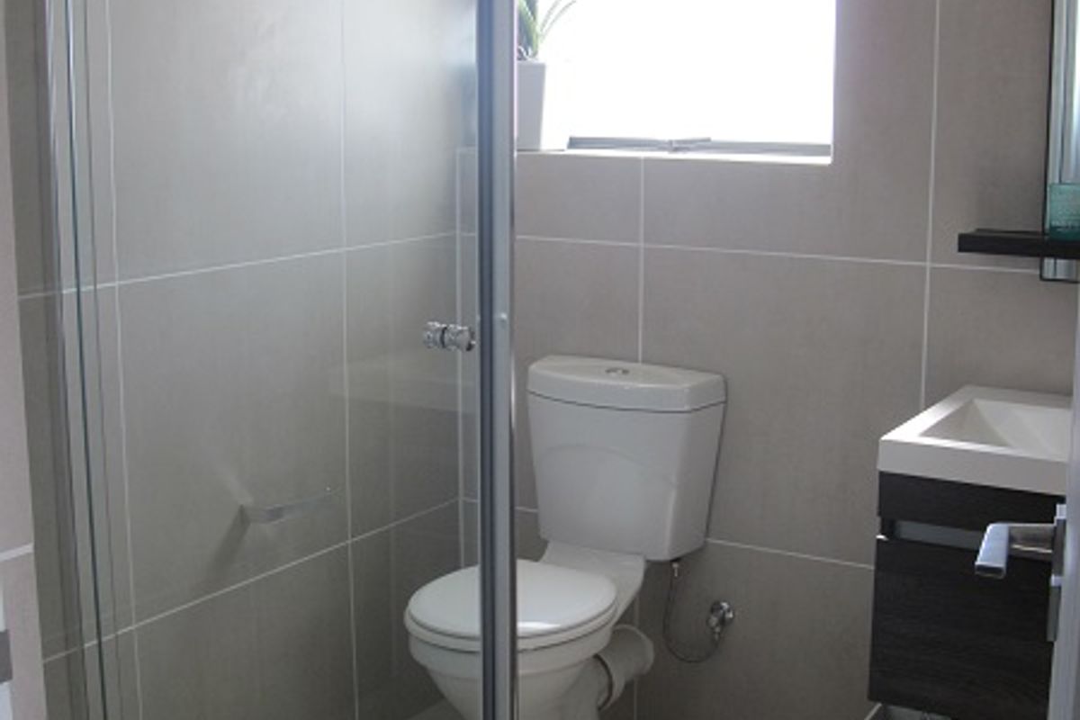 A modern bathroom featuring a glass shower enclosure, a wall-mounted vanity, and neutral ceramic tiling throughout.