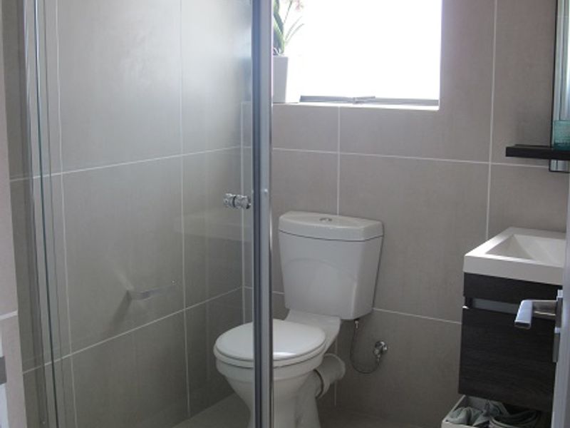 A modern bathroom featuring a glass shower enclosure, a wall-mounted vanity, and neutral ceramic tiling throughout.