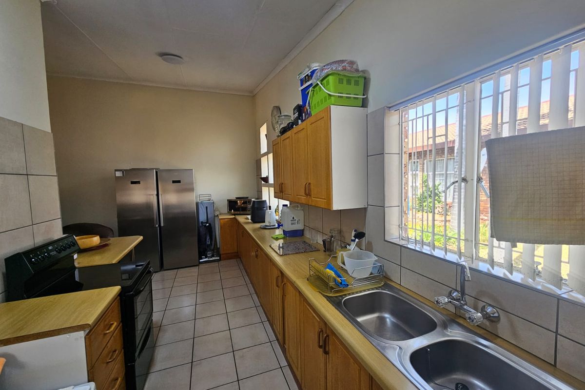 A functional kitchen featuring wooden cabinetry, a double stainless steel sink, tiled flooring, and a built-in stove with ample counter space.