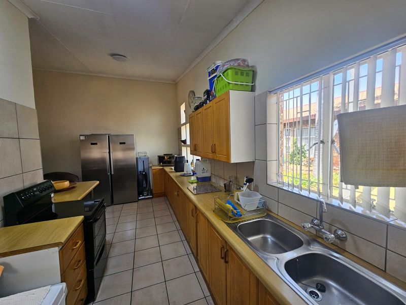 A functional kitchen featuring wooden cabinetry, a double stainless steel sink, tiled flooring, and a built-in stove with ample counter space.