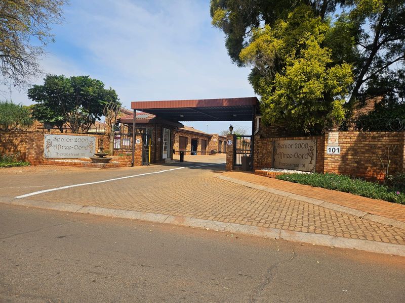 The front entrance of the Senior 2000 Aftree-Oord townhouse complex, featuring a paved driveway, secure gated access, and brick boundary walls.