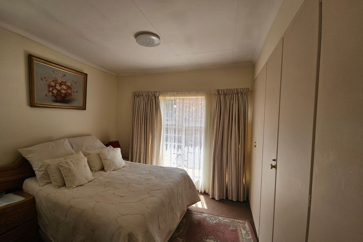 A standard bedroom featuring built-in cupboards, neutral wall finishes, and natural light through a window with curtain rails.