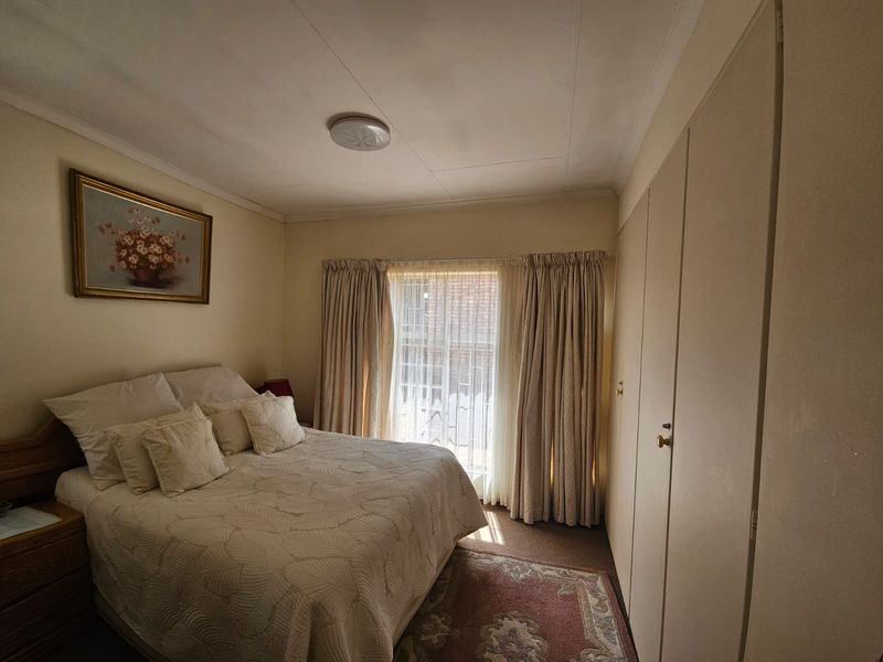 A standard bedroom featuring built-in cupboards, neutral wall finishes, and natural light through a window with curtain rails.