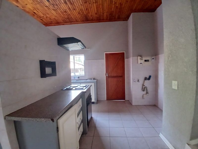 A functional kitchen space featuring built-in cabinetry, a hob, oven, extractor fan, and tiled flooring, with a timber-paneled ceiling.