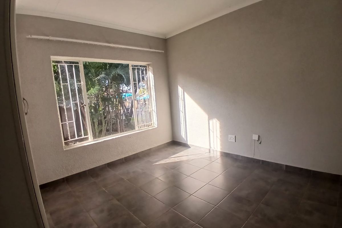 A bright, empty bedroom featuring tiled flooring, built-in cupboard storage, and security bars on the window.