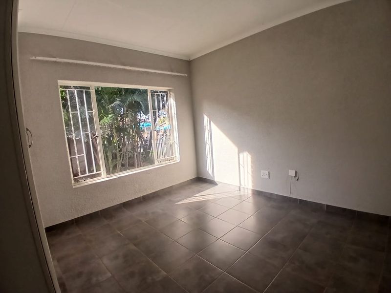 A bright, empty bedroom featuring tiled flooring, built-in cupboard storage, and security bars on the window.