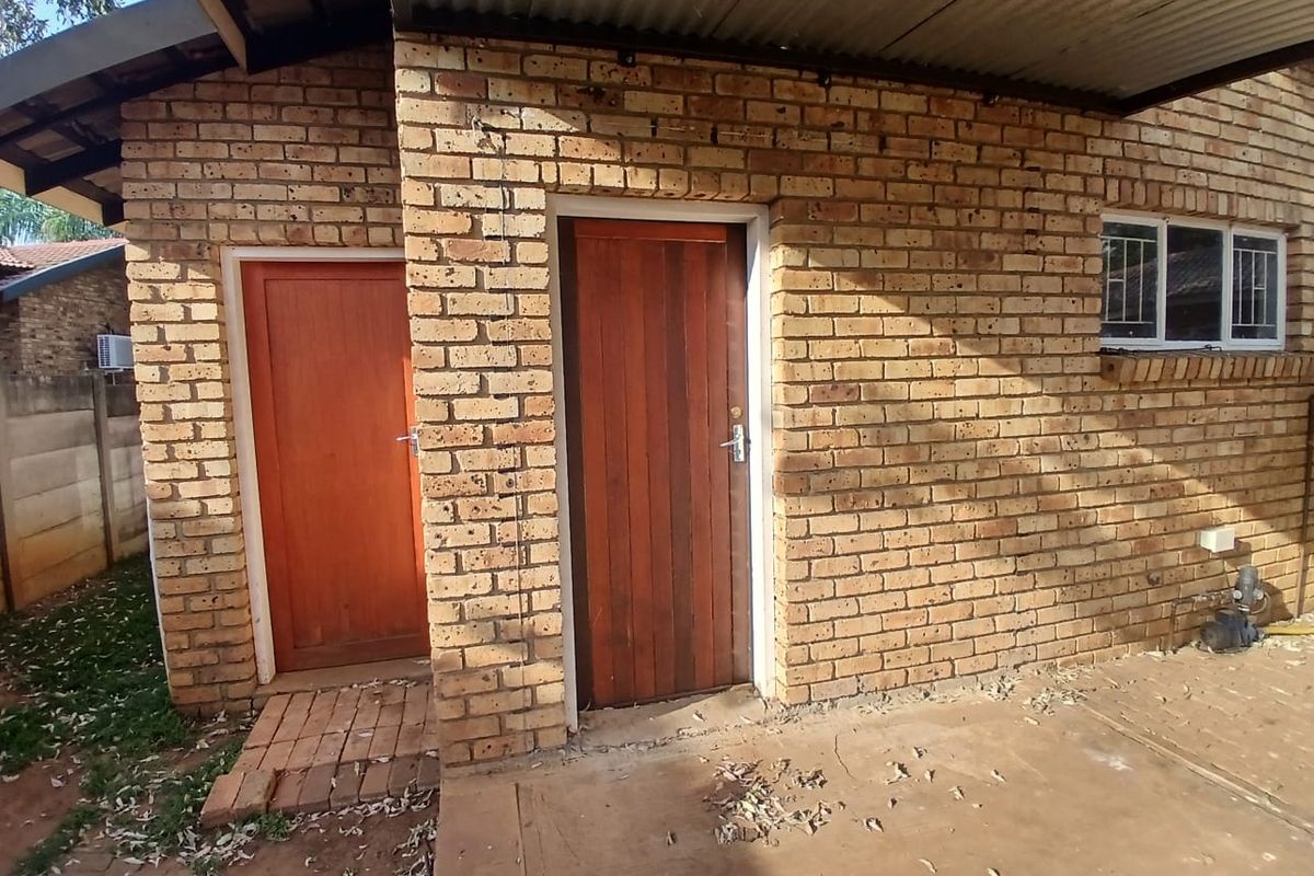 Rear exterior view of the property featuring face brick walls, timber doors, and a covered concrete patio area.
