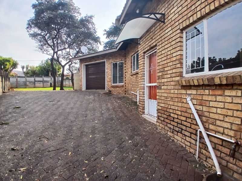 Exterior view of a face brick house featuring a paved driveway, single garage, and security features including burglar bars and a security gate.