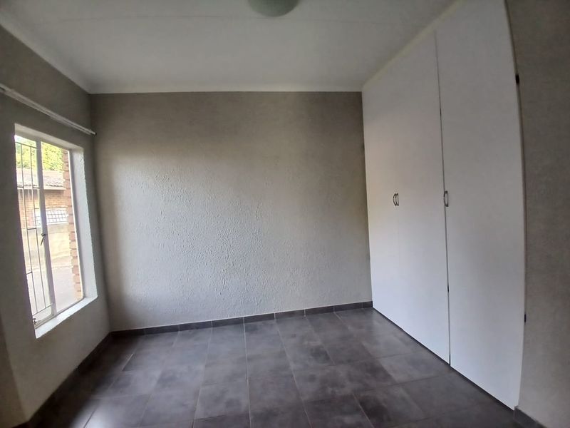 An empty bedroom featuring tiled flooring, built-in cupboards, and a window with security bars.