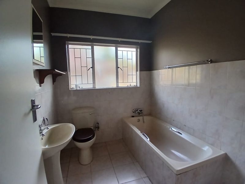 A functional bathroom featuring a pedestal basin, toilet, and bathtub with tiled walls and flooring, ready for modernization.