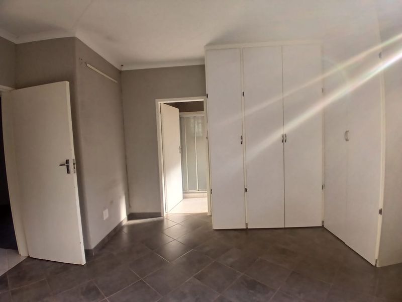 A vacant bedroom featuring neutral wall tones, tiled flooring, and ample built-in cupboard storage, with an adjacent en-suite bathroom visible.