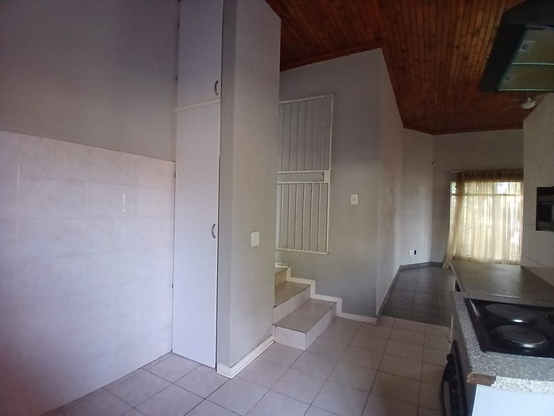 A functional kitchen area featuring tiled flooring, built-in cabinetry, a hob, and a distinctive timber ceiling, leading to an adjacent living space.