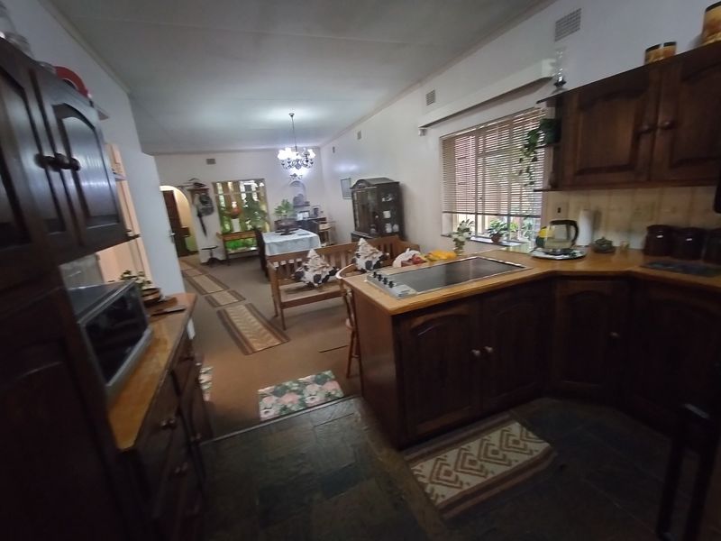 Open plan kitchen and living area featuring traditional dark wood cabinetry, integrated cooktop, and slate flooring in a dated but functional layout.