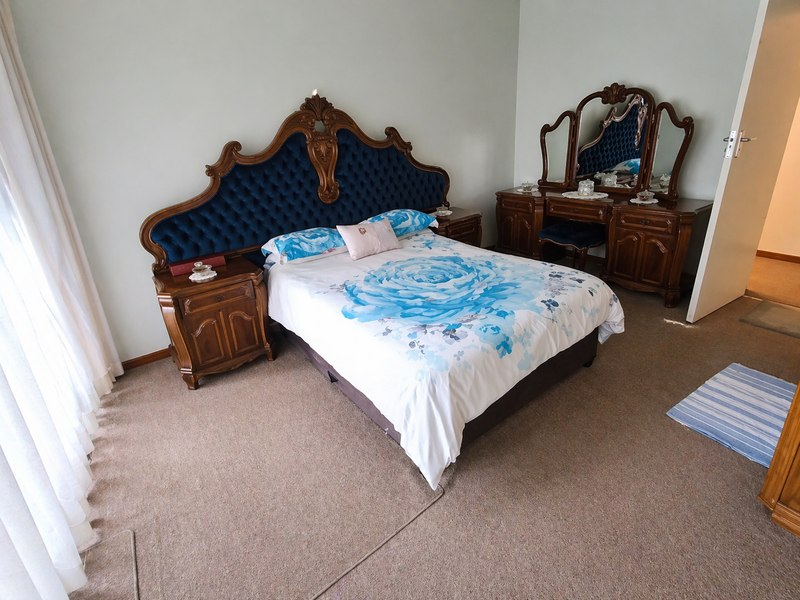 A spacious bedroom featuring neutral wall tones, carpeted flooring, and large windows with curtains, offering a comfortable and functional living space.