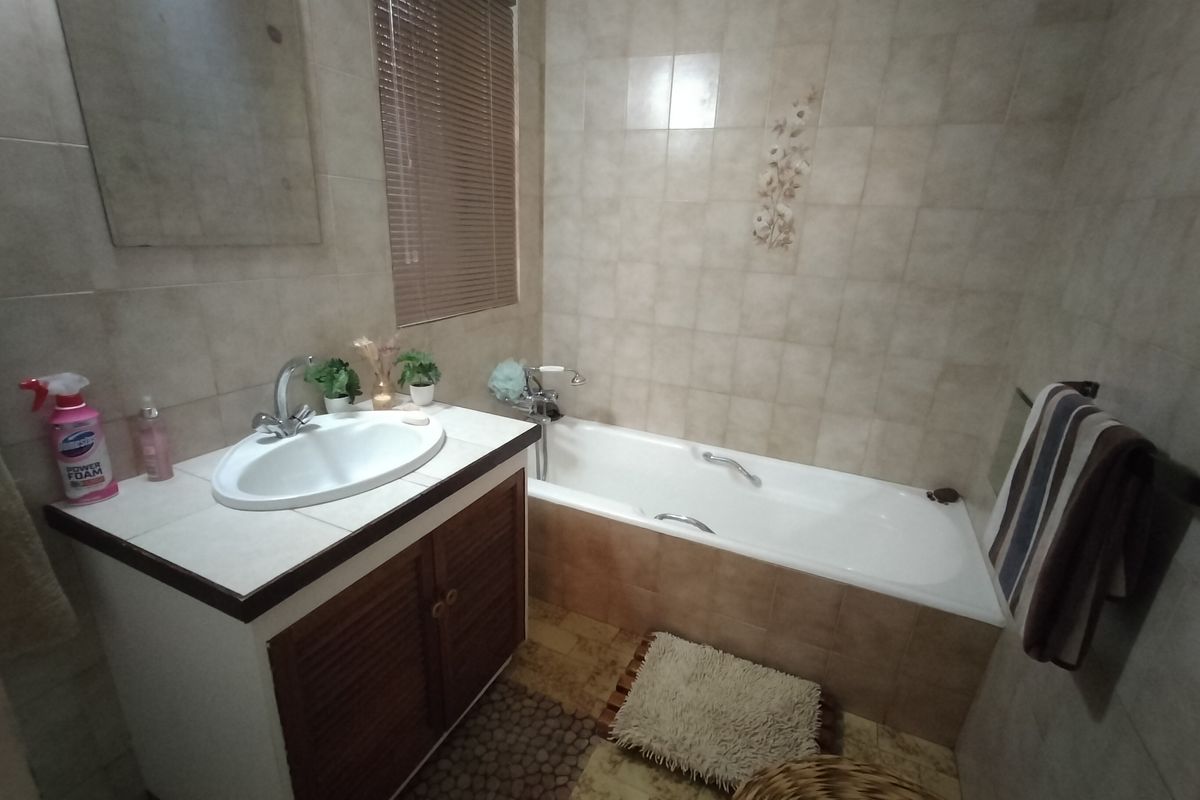 A functional bathroom featuring a vanity cabinet with a drop-in sink, a bathtub with tiled surround, and neutral wall tiling.