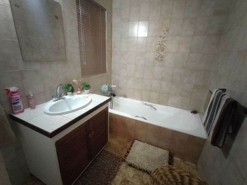 A functional bathroom featuring a vanity cabinet with a drop-in sink, a bathtub with tiled surround, and neutral wall tiling.