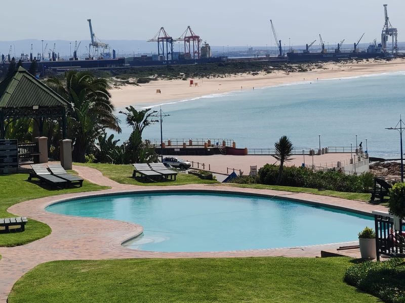 Outdoor swimming pool area featuring a paved surround, gazebo, and landscaped garden with scenic coastal and harbour views.