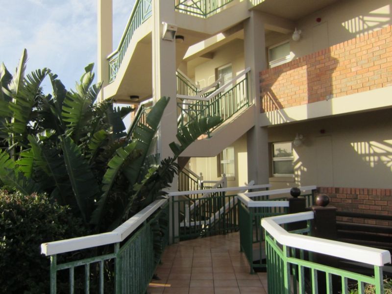 Exterior view of an apartment complex featuring a tiled walkway, staircase, and brick facade with metal railings.