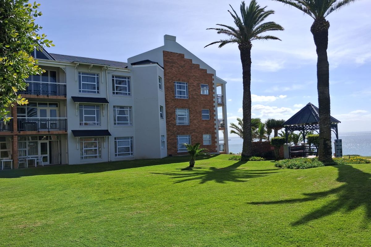 A view of the apartment building's rear facade featuring brick detailing, private balconies, and a well-maintained lawn with a gazebo overlooking the ocean.
