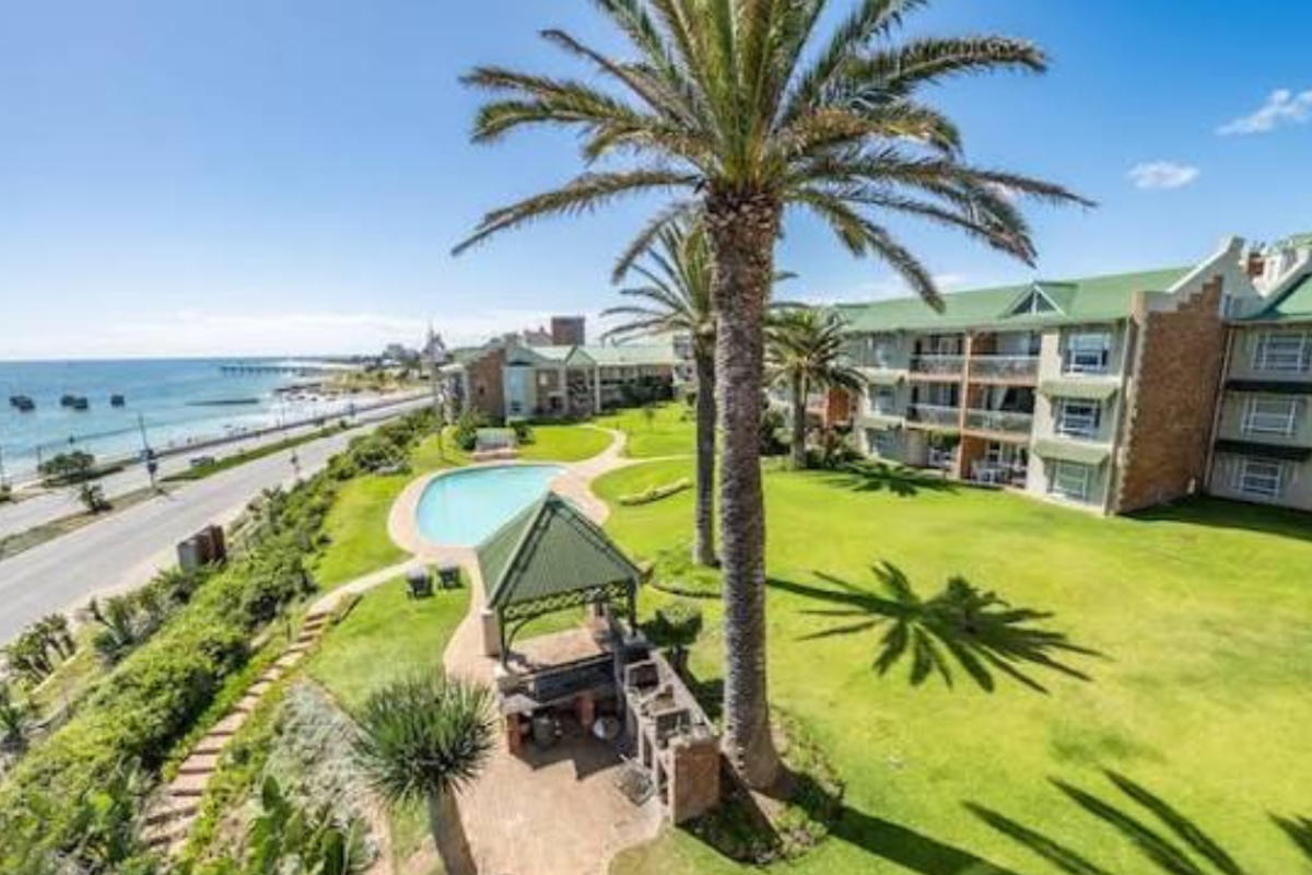 Aerial view of the apartment complex grounds featuring a swimming pool, communal gazebo with built-in braai, landscaped gardens, and ocean views.
