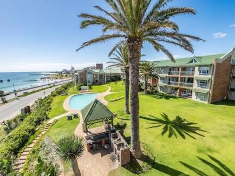 Aerial view of the apartment complex grounds featuring a swimming pool, communal gazebo with built-in braai, landscaped gardens, and ocean views.