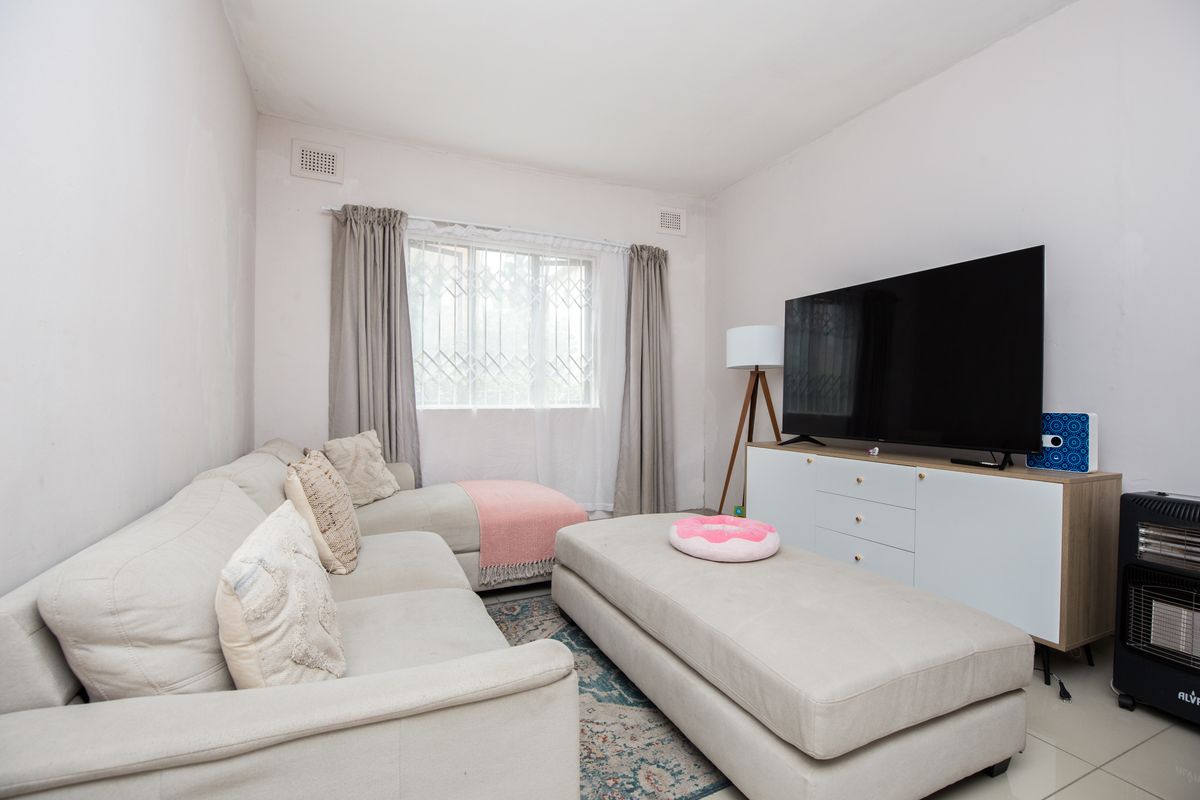 A living room featuring tiled flooring, a window with security bars, and wall-mounted ventilation grilles.