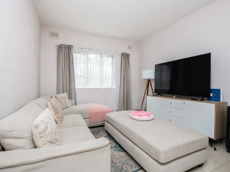 A living room featuring tiled flooring, a window with security bars, and wall-mounted ventilation grilles.