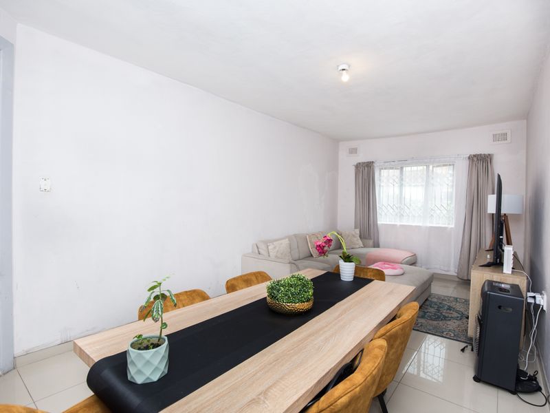Open plan living and dining area featuring tiled flooring and a window with security bars, offering a functional space for daily living.