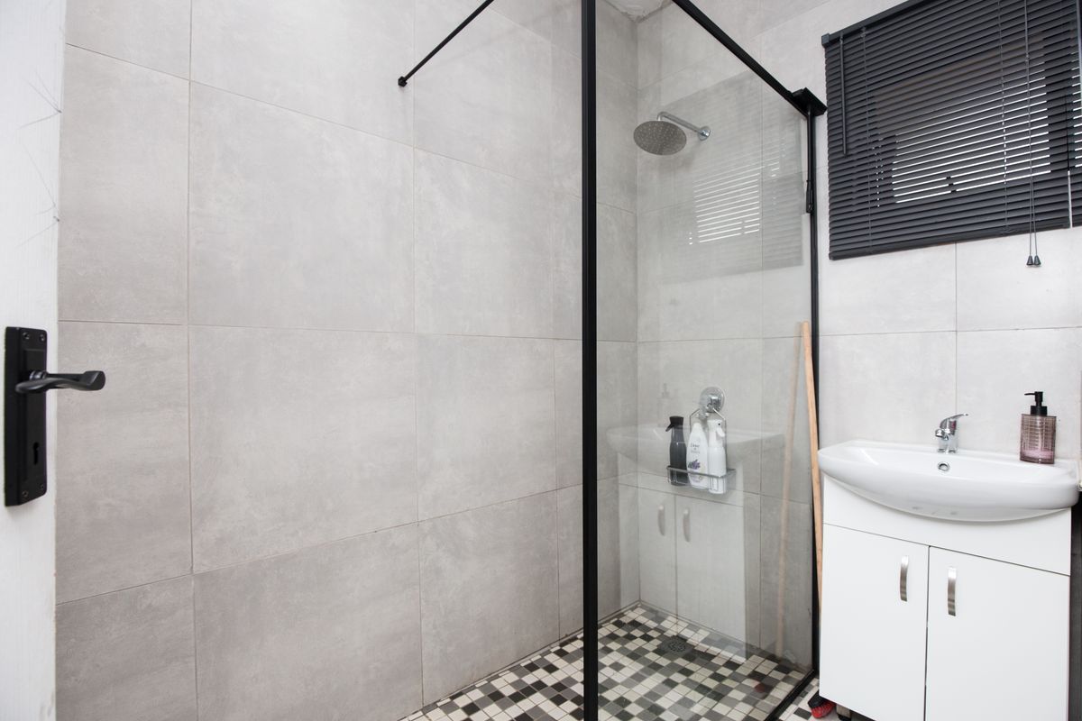 Modern bathroom featuring a walk-in shower with a black-framed glass screen, mosaic floor tiling, and a white vanity basin with storage cabinet.