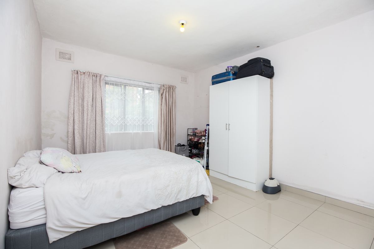 A bedroom featuring tiled flooring, a window with security bars, and ventilation grilles, showing signs of wall wear and paint deterioration.
