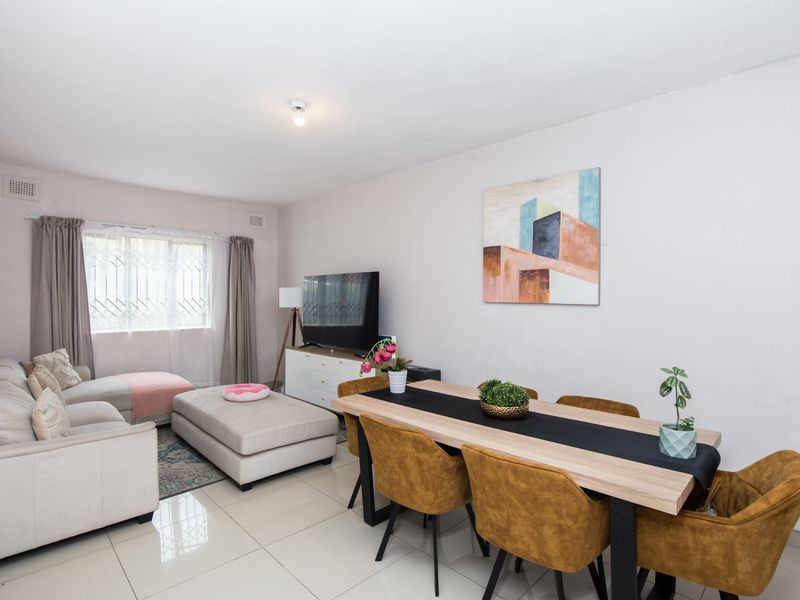 An open-plan living and dining area featuring neutral tiled flooring, large windows with security bars, and a functional layout suitable for modern living.