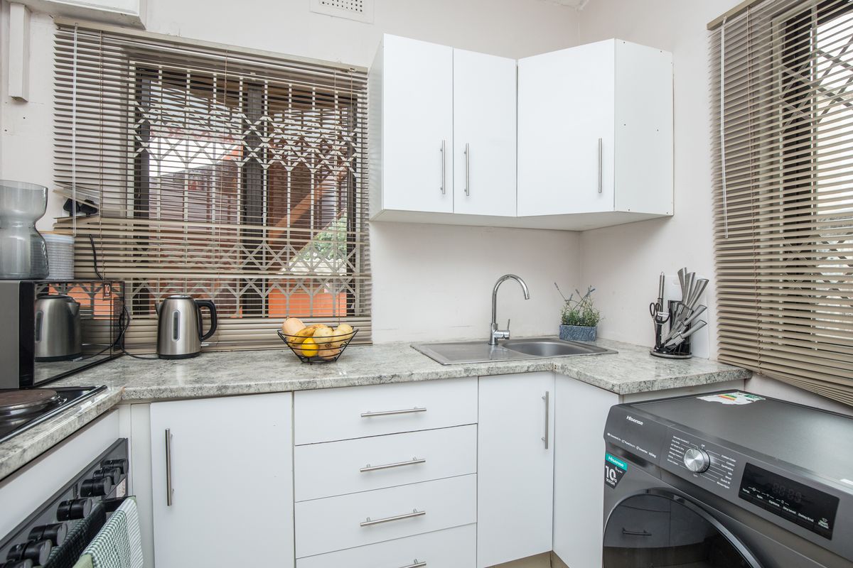 Compact kitchen featuring white cabinetry, laminate countertops, stainless steel sink, and integrated space for a washing machine.