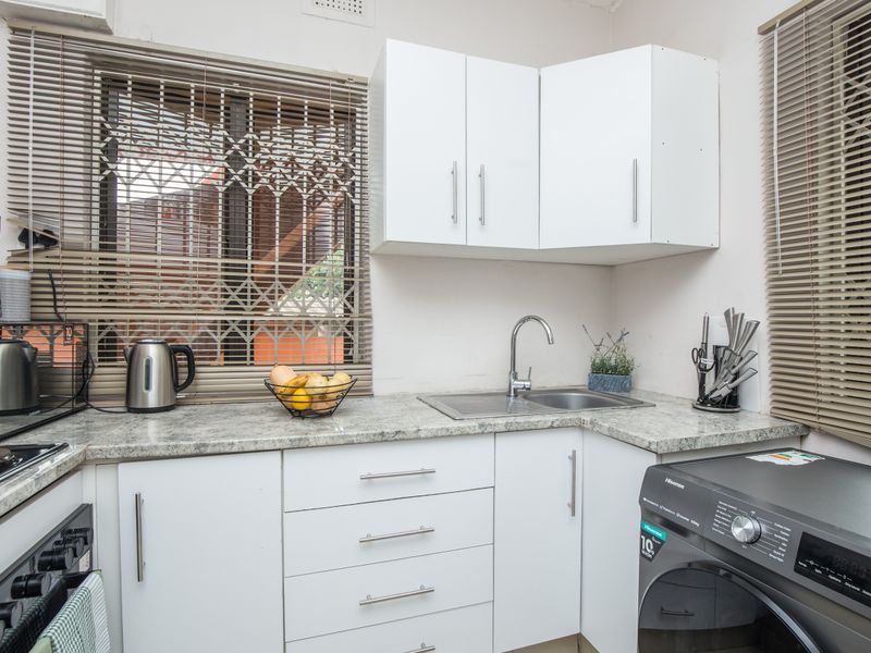 Compact kitchen featuring white cabinetry, laminate countertops, stainless steel sink, and integrated space for a washing machine.
