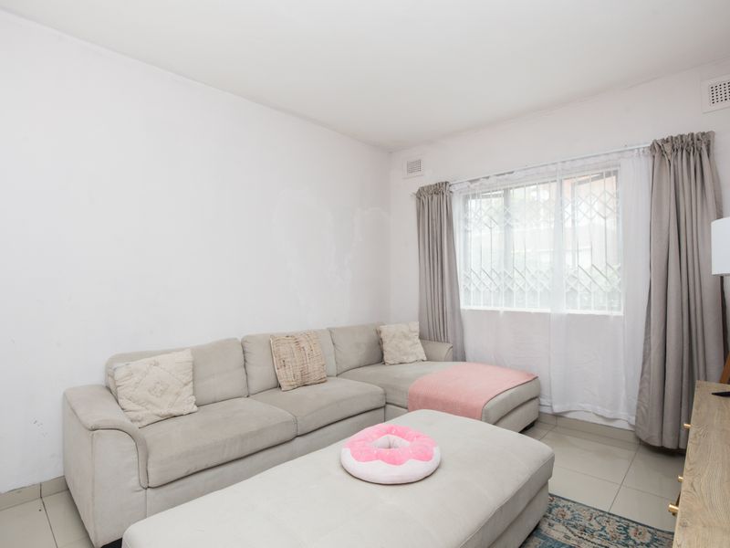 A living room featuring tiled flooring, a window with a security gate, and ventilation grilles.