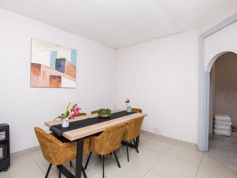 Dining area featuring tiled flooring and an arched doorway, showing visible signs of wall wear and plaster damage requiring maintenance.